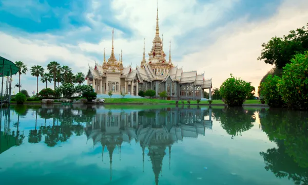 Grand Thai temple with ornate golden spires, beautifully reflected in a tranquil pond at sunset, surrounded by lush greenery – Asia Cruises, Luxury Sassy Cruises.