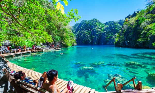 Travelers relax by the crystal-clear turquoise waters of a secluded lagoon surrounded by dramatic limestone cliffs and lush greenery in Palawan, Philippines, a highlight of luxury Asia cruises.