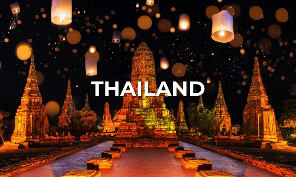 Nighttime view of ancient Thai temple ruins illuminated by floating lanterns during a festival.