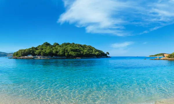 Tranquil Caribbean island surrounded by crystal-clear turquoise waters and lush green foliage, under a vibrant blue sky - perfect tropical escape.