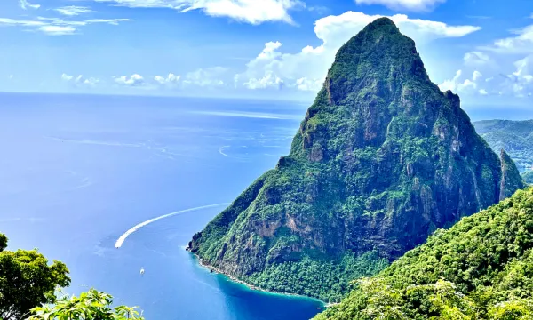 Majestic view of the Pitons in St. Lucia—lush green mountain rising above the turquoise Caribbean Sea, with dramatic coastline and a blue sky.