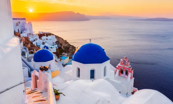 Whitewashed buildings with blue domes overlooking the Aegean Sea at sunset in Santorini, Greece – a signature view from a luxury Mediterranean cruise.