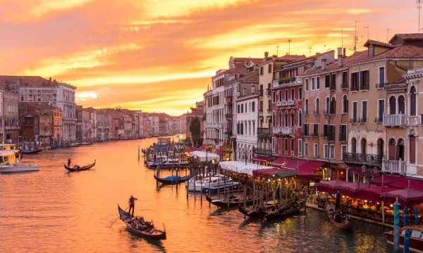 Sunrise view of Venice's Grand Canal with gondolas drifting past historic buildings and vibrant waterside cafés.