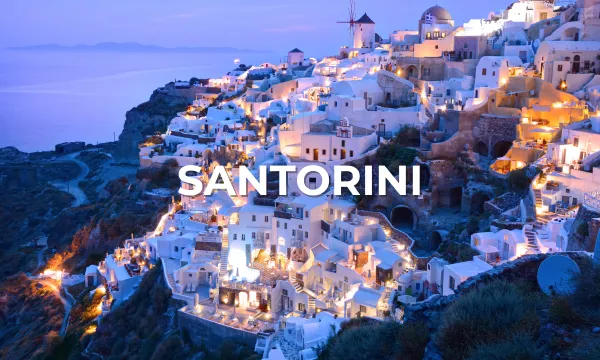 Iconic whitewashed cliffside buildings of Santorini glowing at sunset, with blue-domed churches and the Aegean Sea.