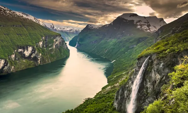 A luxury cruise ship sails through Norway’s spectacular Geirangerfjord, surrounded by towering cliffs, cascading waterfalls, and the timeless beauty of Northern Europe’s wild landscapes.