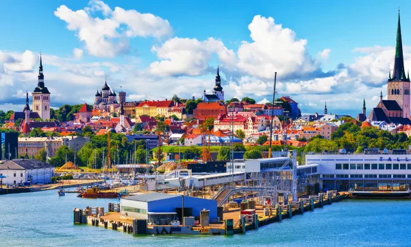 A vibrant summer view of Tallinn’s historic skyline and colorful old town, seen from the harbor with cruise docks and marina in the foreground.