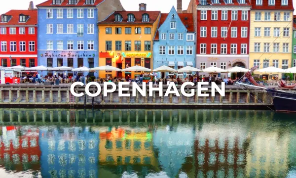 Charming colourful townhouses line the Nyhavn waterfront in Copenhagen, with outdoor cafés and their reflections mirrored in the peaceful canal.