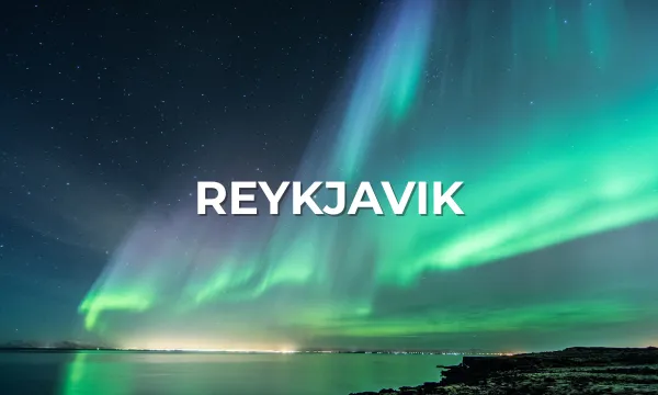 The Northern Lights dance over Reykjavik's coastal skyline, illuminating the sky with green and purple hues above a glowing Icelandic shoreline.