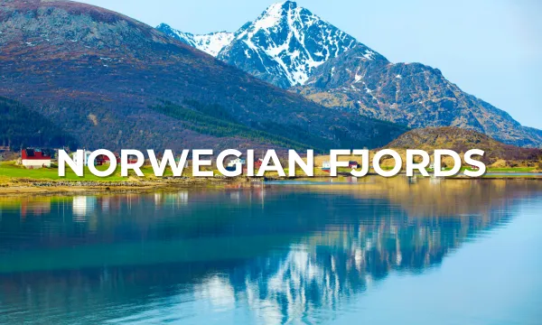 Stunning view of the Norwegian fjords with snow-capped mountains reflected in calm blue water and a quaint red cabin nestled on the shoreline.