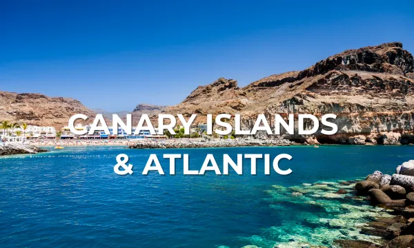 A vivid coastal scene with clear turquoise water, rugged volcanic cliffs, and a sunny blue sky in the Canary Islands, showcasing an inviting cruise destination in the Atlantic. White text reads "Canary Islands & Atlantic."