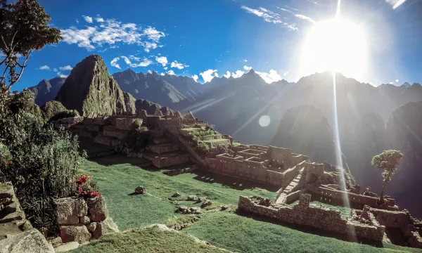 Machu Picchu’s ancient Inca stone terraces and temples bathed in the golden rays of a rising sun, with the Andes peaks silhouetted against a clear blue sky.
