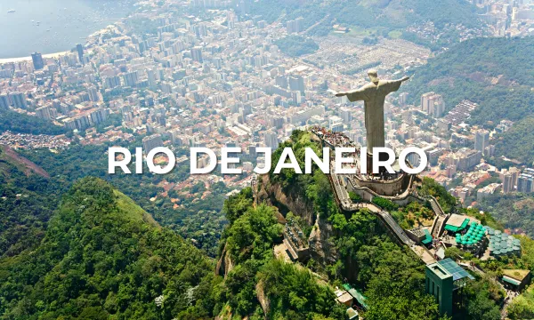 Aerial view from Corcovado Mountain showing the Christ the Redeemer statue overlooking Rio de Janeiro’s high-rise skyline, Guanabara Bay and Sugarloaf Mountain in the distance.