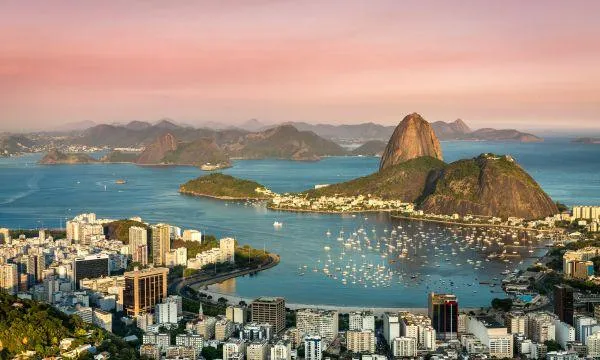 A panoramic view of Rio de Janeiro’s iconic Sugarloaf Mountain and Guanabara Bay at sunset, with sailboats in the harbour – a highlight stop on an Azamara South America cruise.