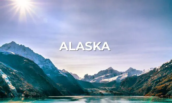 Snow-capped Alaskan mountains reflecting in turquoise waters under a bright sun – an iconic scene from an Azamara boutique Alaska cruise.