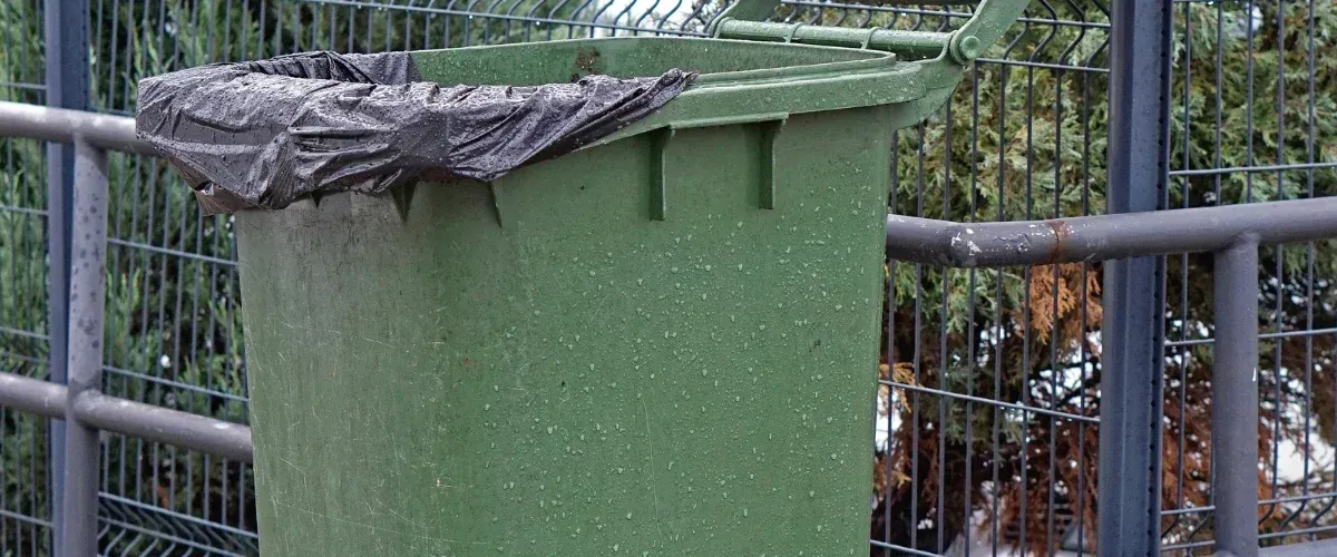 A close-up of a green plastic bin with a black trash liner over its rim, covered in water droplets.