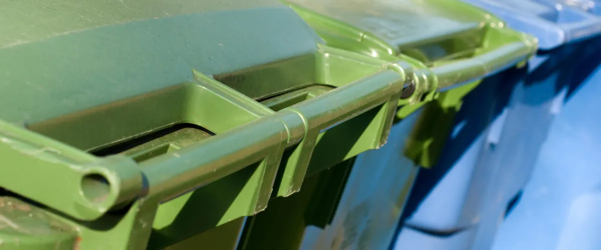 A close-up view of the connected green and blue lids of two plastic recycling bins in sunlight.