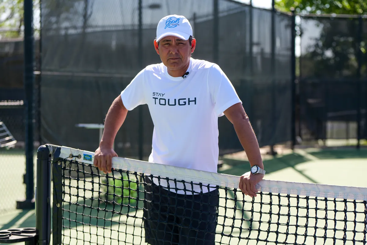 Coach Julian Lopez at the net on a hard court