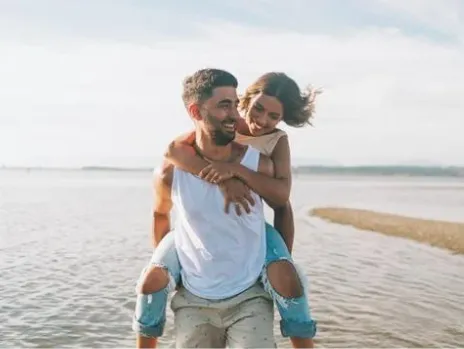 Smiling couple enjoying a piggyback ride on the beach, symbolizing vitality and energy restoration through NAD+ therapy supporting cellular health, DNA repair, and metabolism.