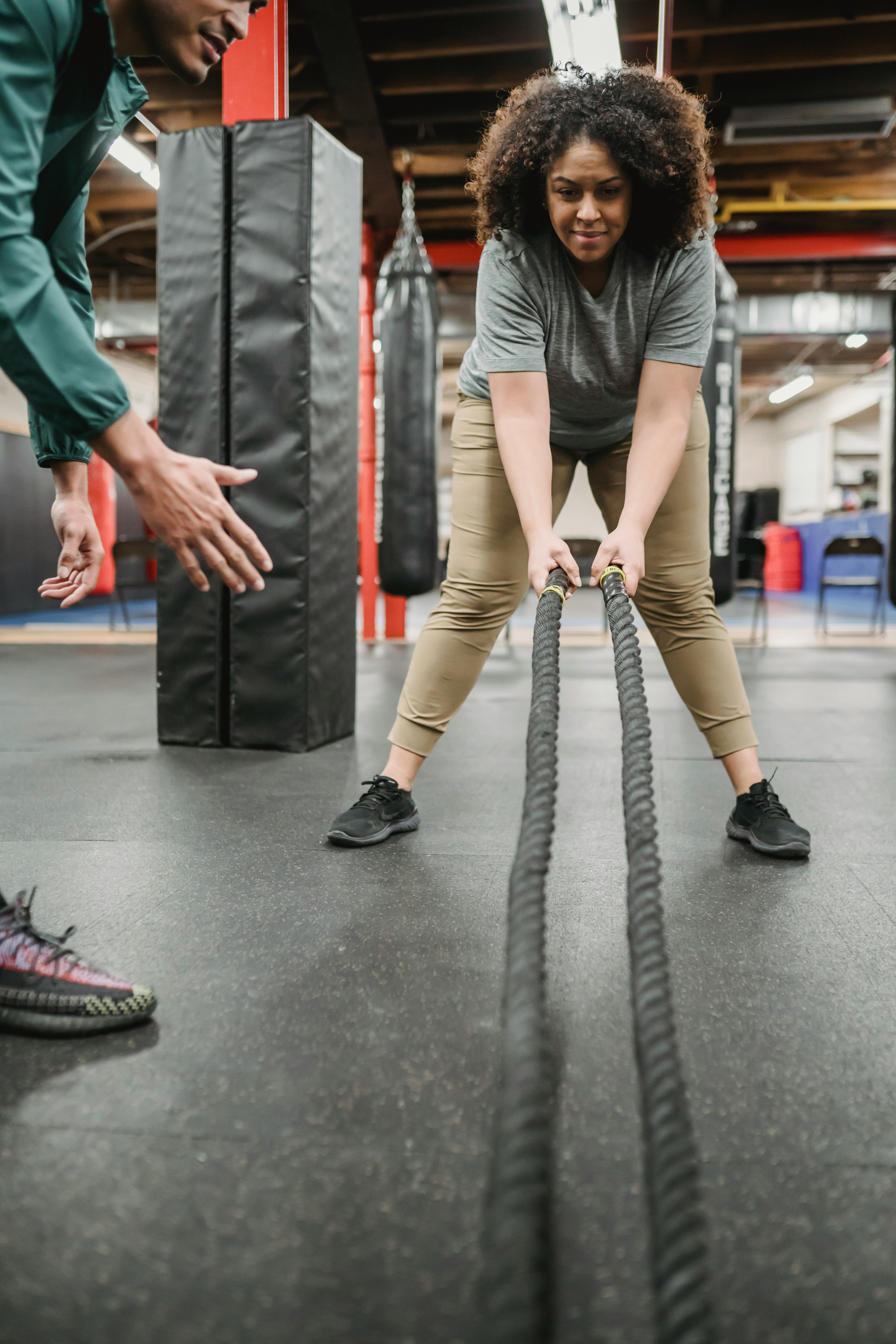 Woman performing battle rope exercises with a trainer in a gym, representing strength, recovery, fitness, and body composition goals.