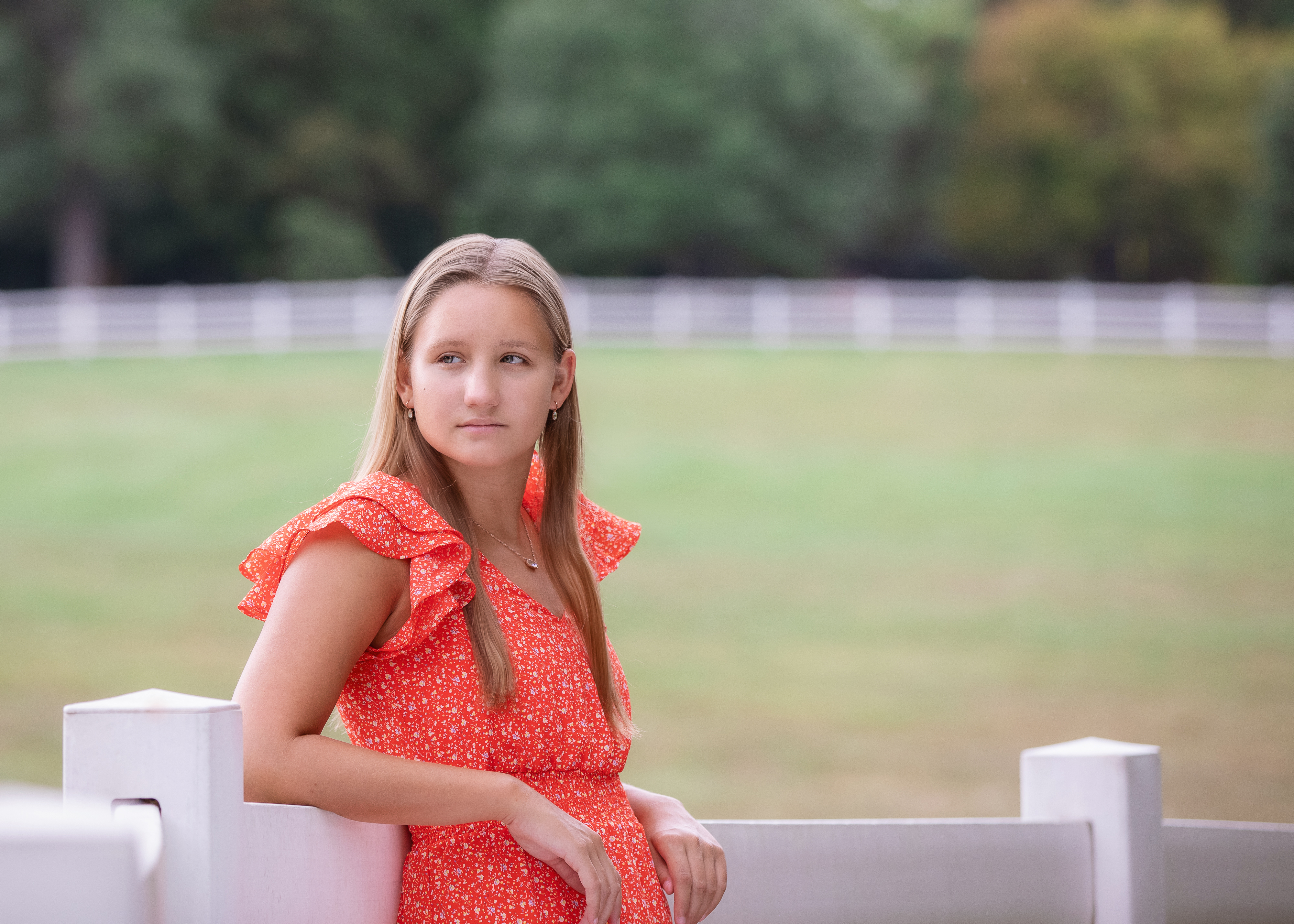 High school senior girl portrait session in Missouri leaning on a fence in a park wearing a coral dress