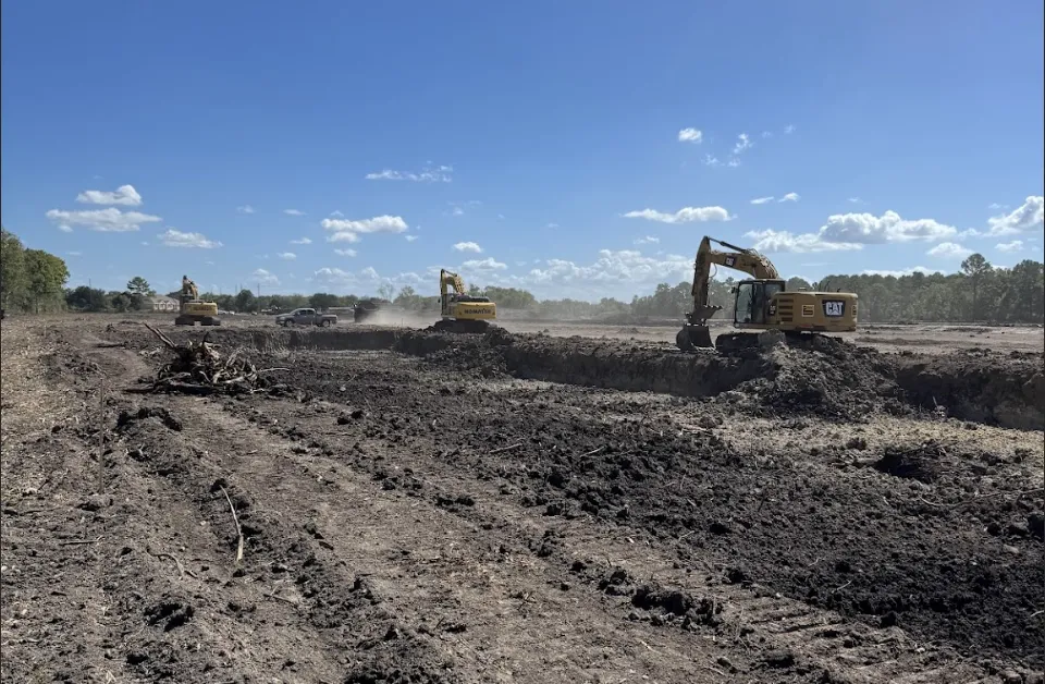 A yellow excavator is digging near a white car.