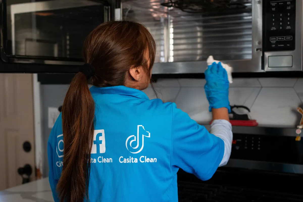 Casita Clean team member wiping down a microwave interior during a deep clean in a suburban kitchen