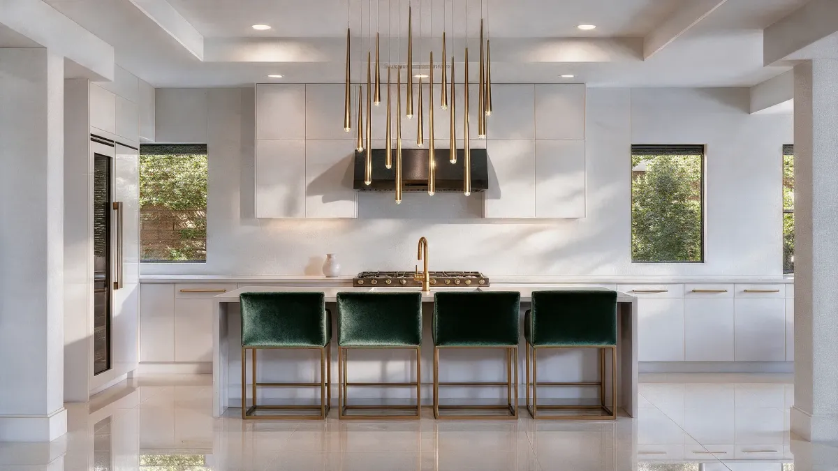 Modern minimalist white kitchen with a large island, deep green velvet counter stools and a brass Modern Forms chandelier, Las Vegas.