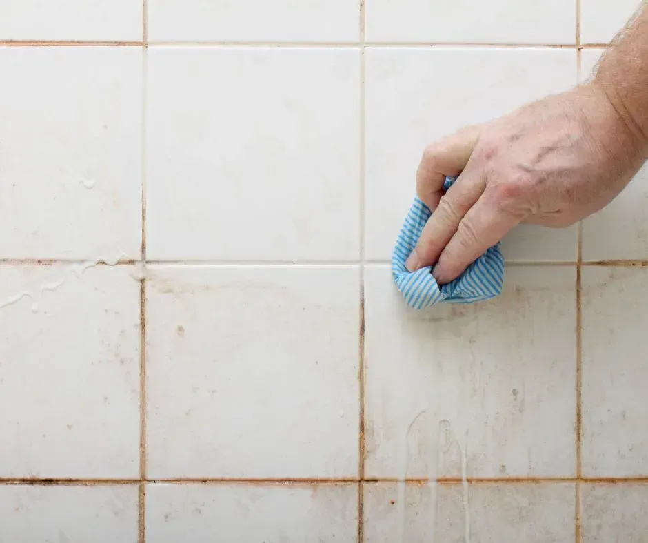 Person scrubbing stained fiberglass shower tile, highlighting worn and discolored bathroom finishes needing replacement.