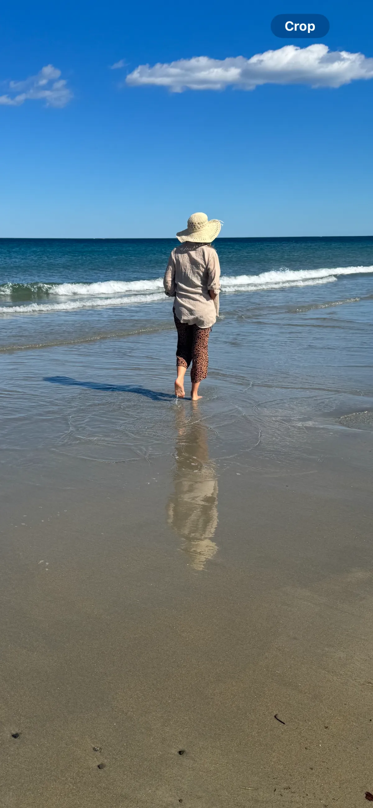 Kandice walking along the ocean shore in a sun hat.