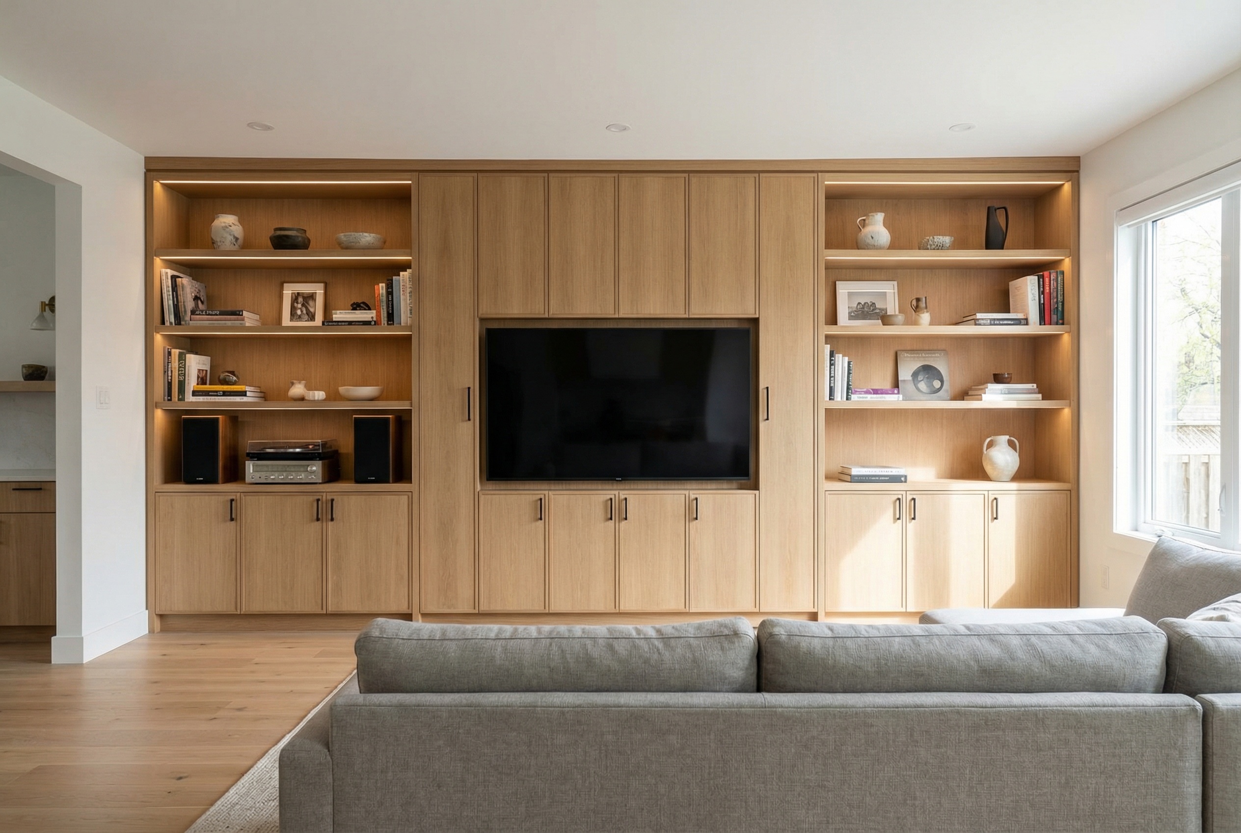 Custom built-in entertainment center with floor-to-ceiling cabinetry, centered TV, and open shelving in a modern living room
