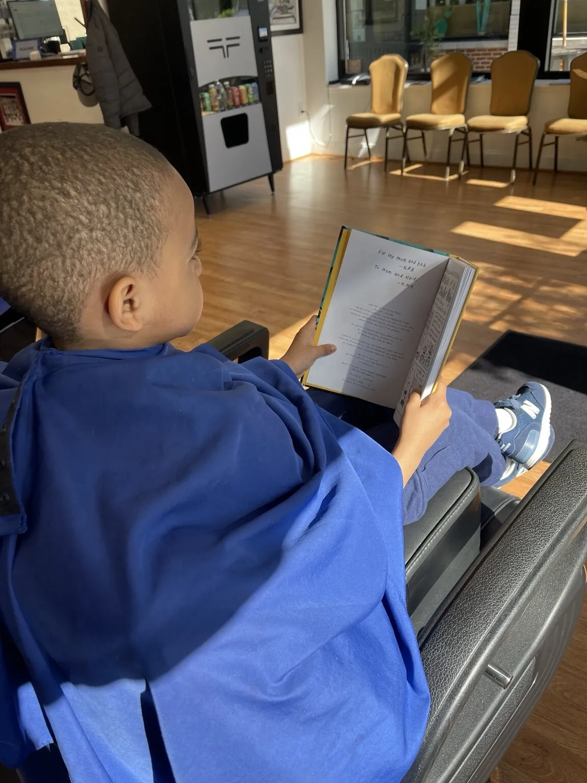 Young child reading comfortably during a haircut at The Ultimate Barber in Alexandria, Virginia
