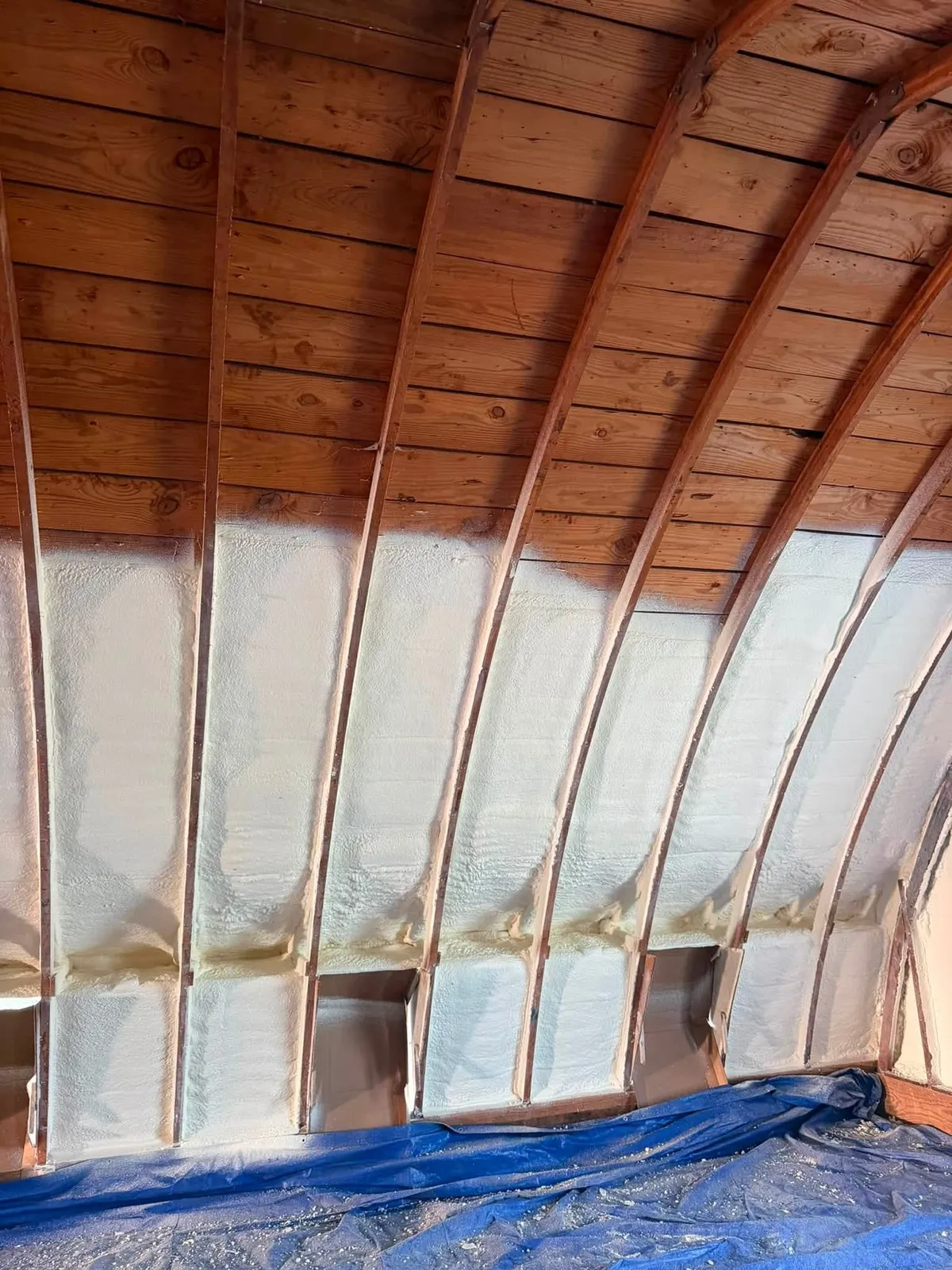 Rigid closed cell spray foam smoothed flat between the rafters of a barn