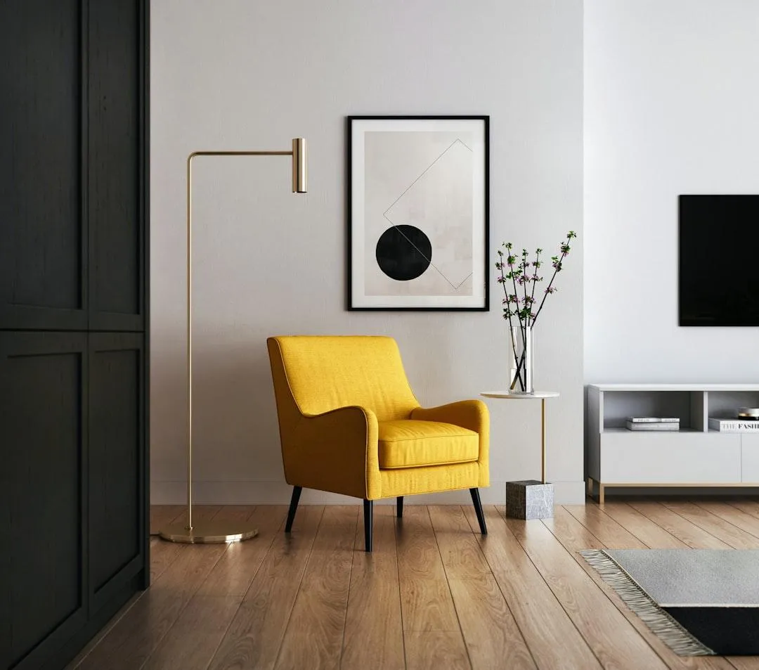 Bright yellow armchair with modern design, gold floor lamp, abstract wall art, small side table with vase, and minimalist TV stand in a stylish living room setting, reflecting contemporary interior design aesthetics.