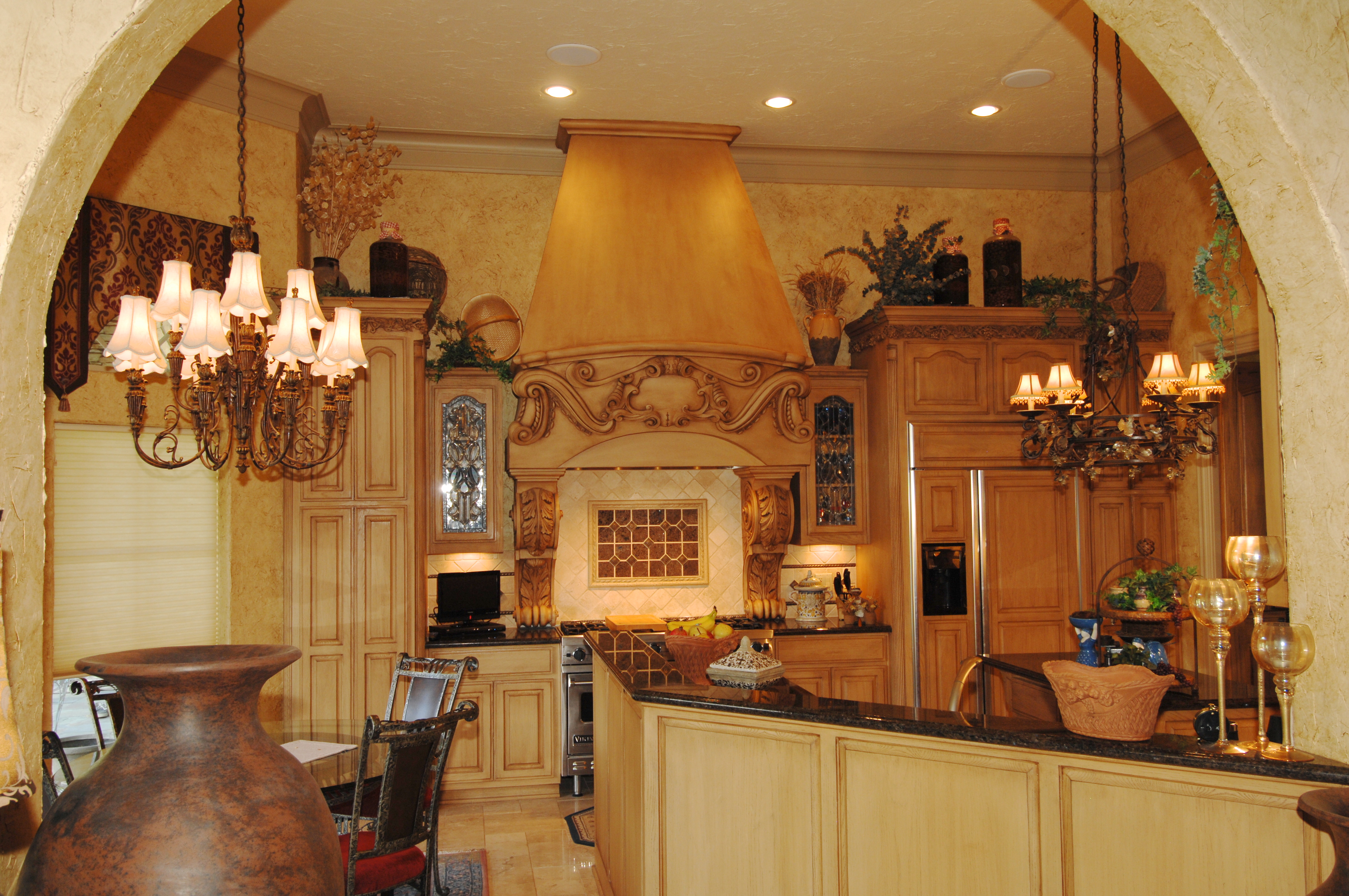 Elegant kitchen interior design featuring custom cabinetry, decorative hood, chandelier lighting, and a blend of warm colors, showcasing DHD Interior Designs' expertise in creating personalized spaces.