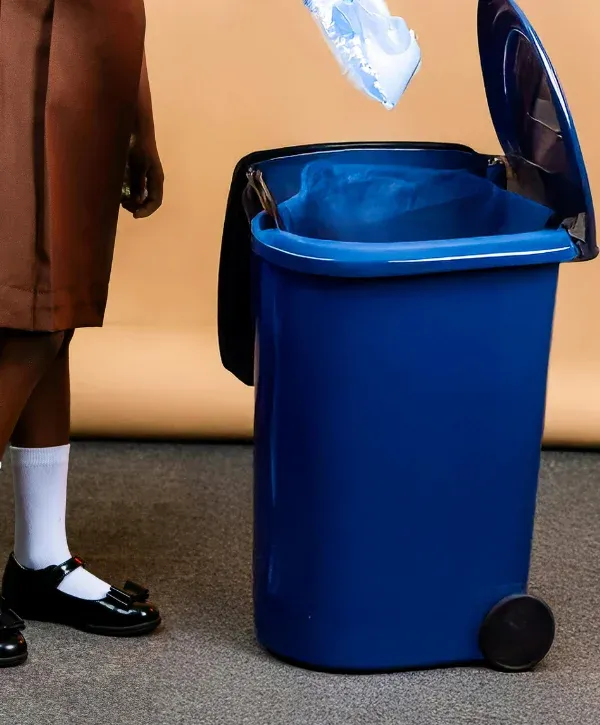 A child in school uniform is shown dropping a plastic item into a blue garbage can with an open lid.