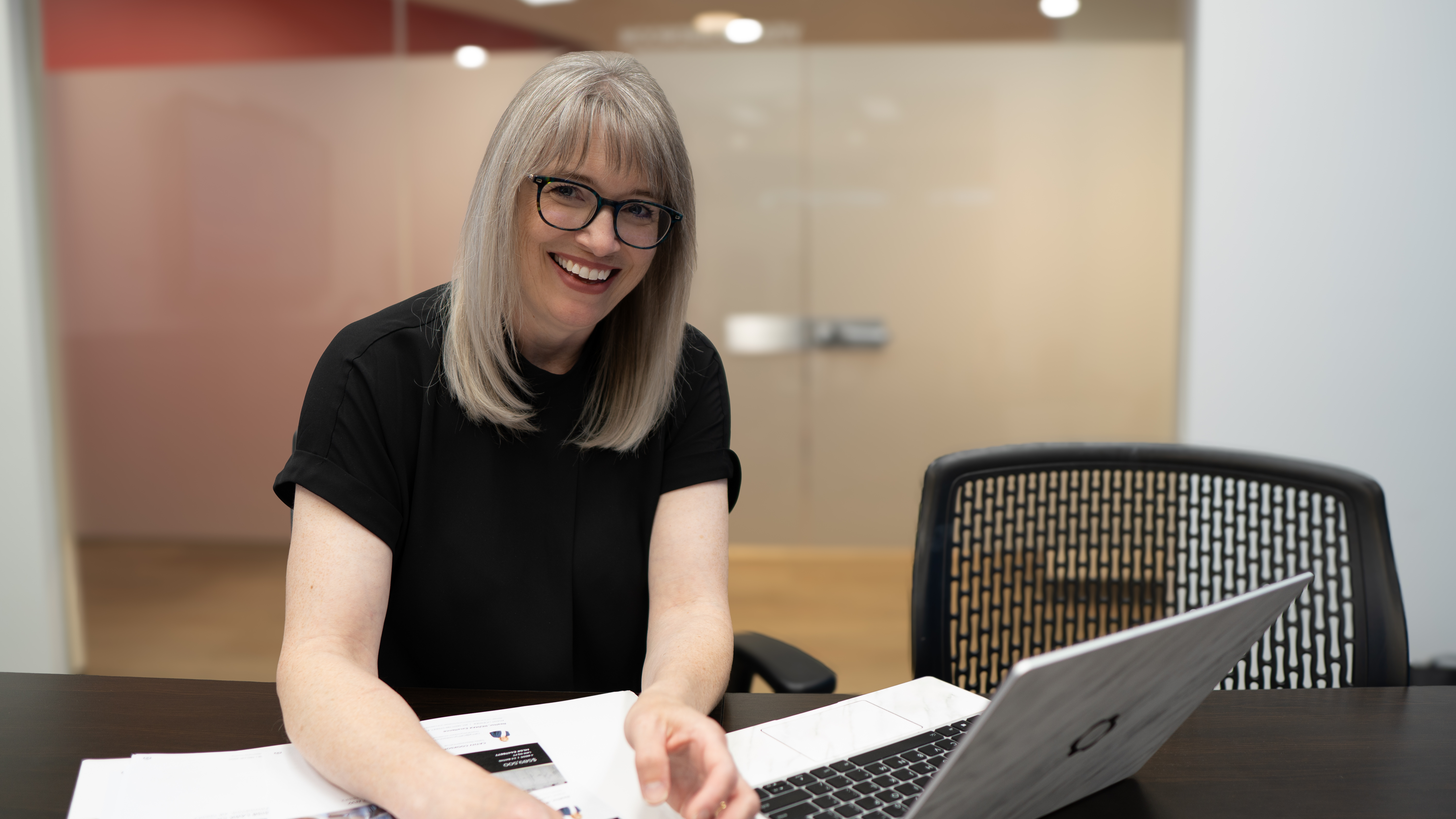 Edmonton realtor Cathy Cookson smiling at her desk, with a laptop and paperwork in front of her.