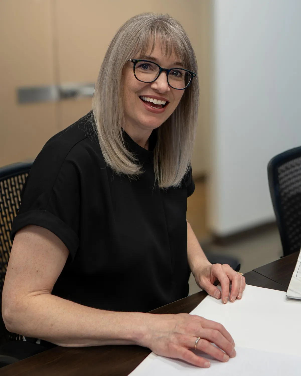 Cathy Cookson smiling at a meeting table in her office, with paperwork in front of her.