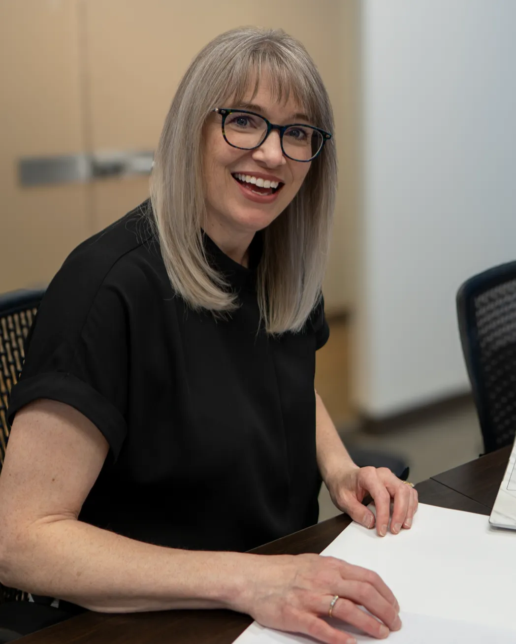 Cathy Cookson smiling at a meeting table in her office, with paperwork in front of her.