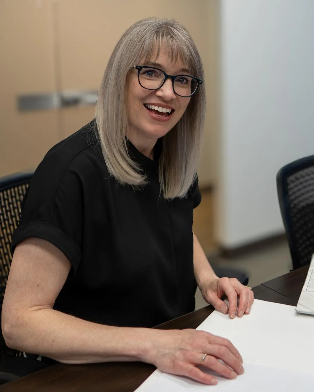 Cathy Cookson smiling at a meeting table in her office, with paperwork in front of her.