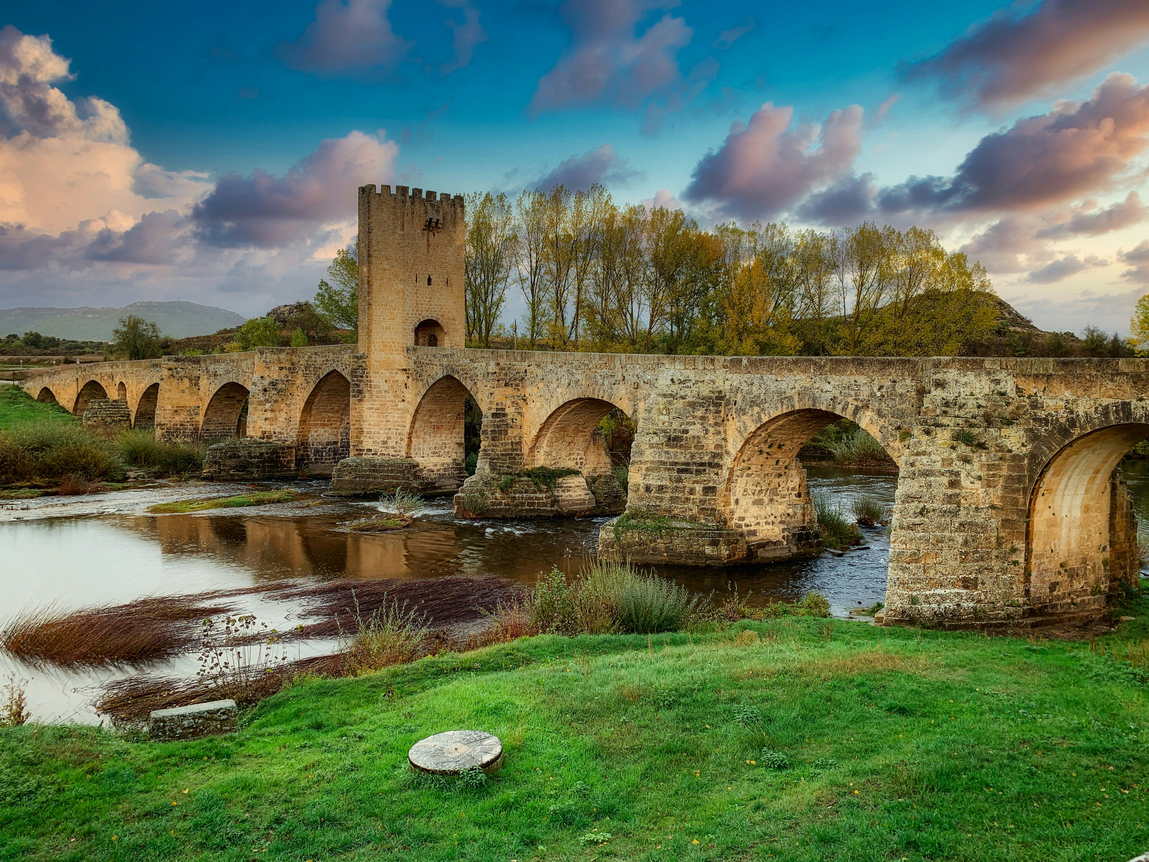 a medieval bridge over a river with clouds above