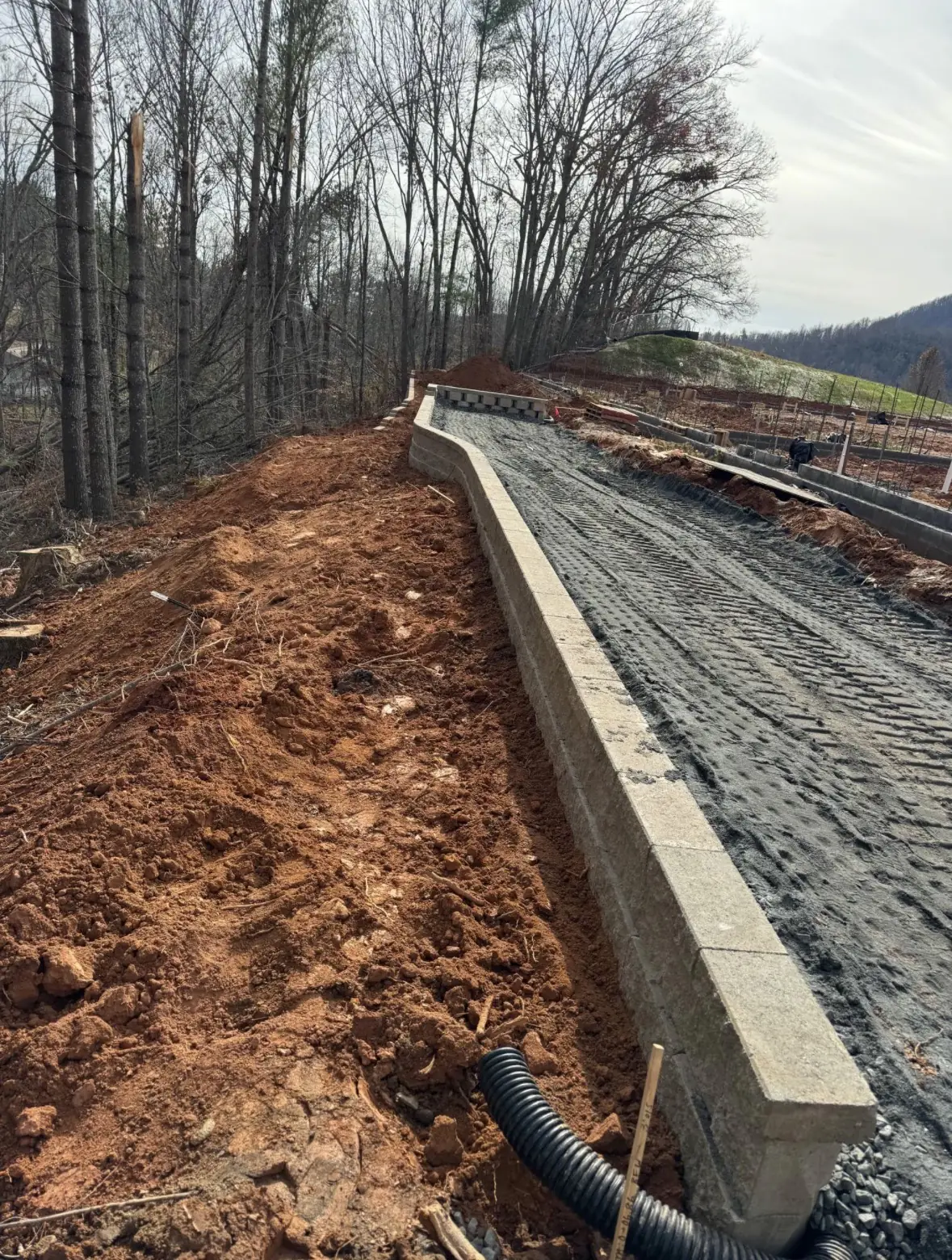 Segmental block retaining wall under construction with drainage pipe, gravel backfill and geogrid