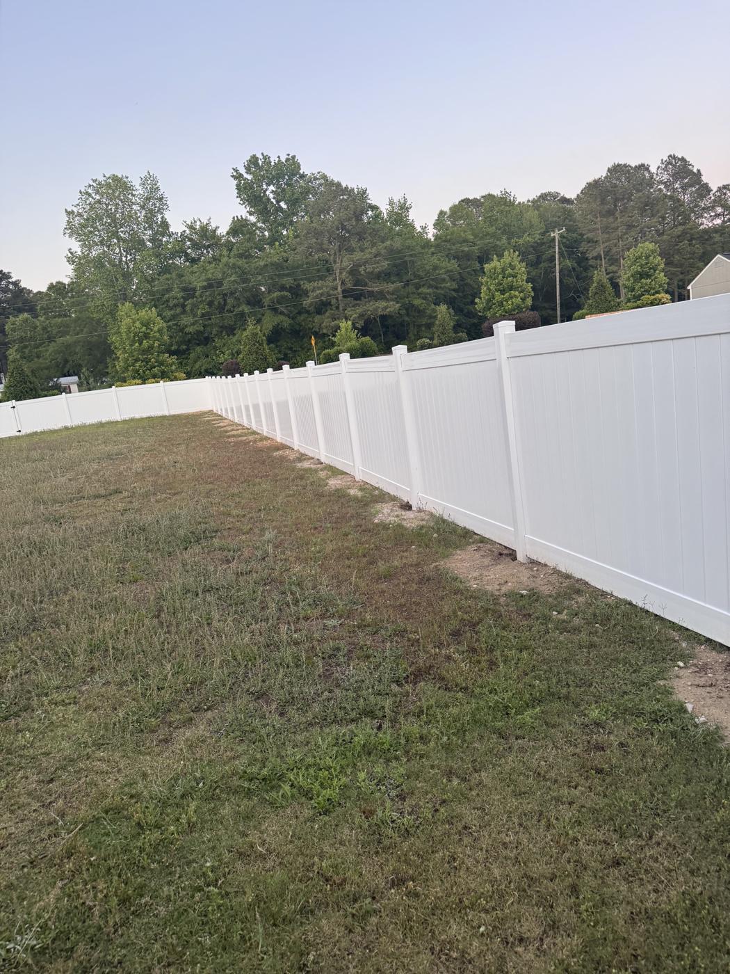 White vinyl privacy fence enclosing large backyard with trees beyond in Lillington, NC