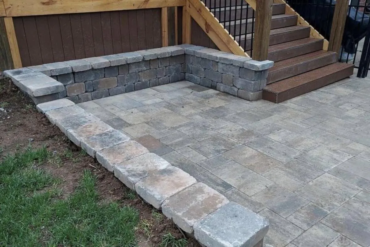 Gray paver patio with block seat wall beside wood deck stairs in the Triangle, NC