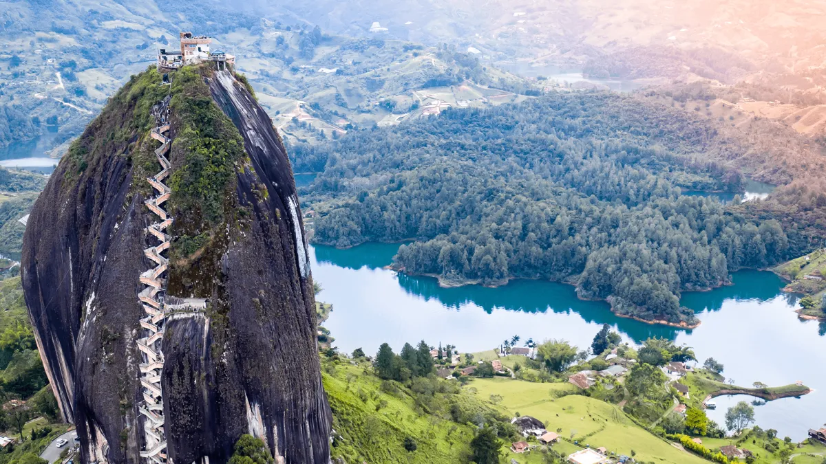 Pareja extranjera en ciudad colombiana, sonriendo, sosteniendo maletas, fondo de arquitectura local, ambiente soleado, estilo realista