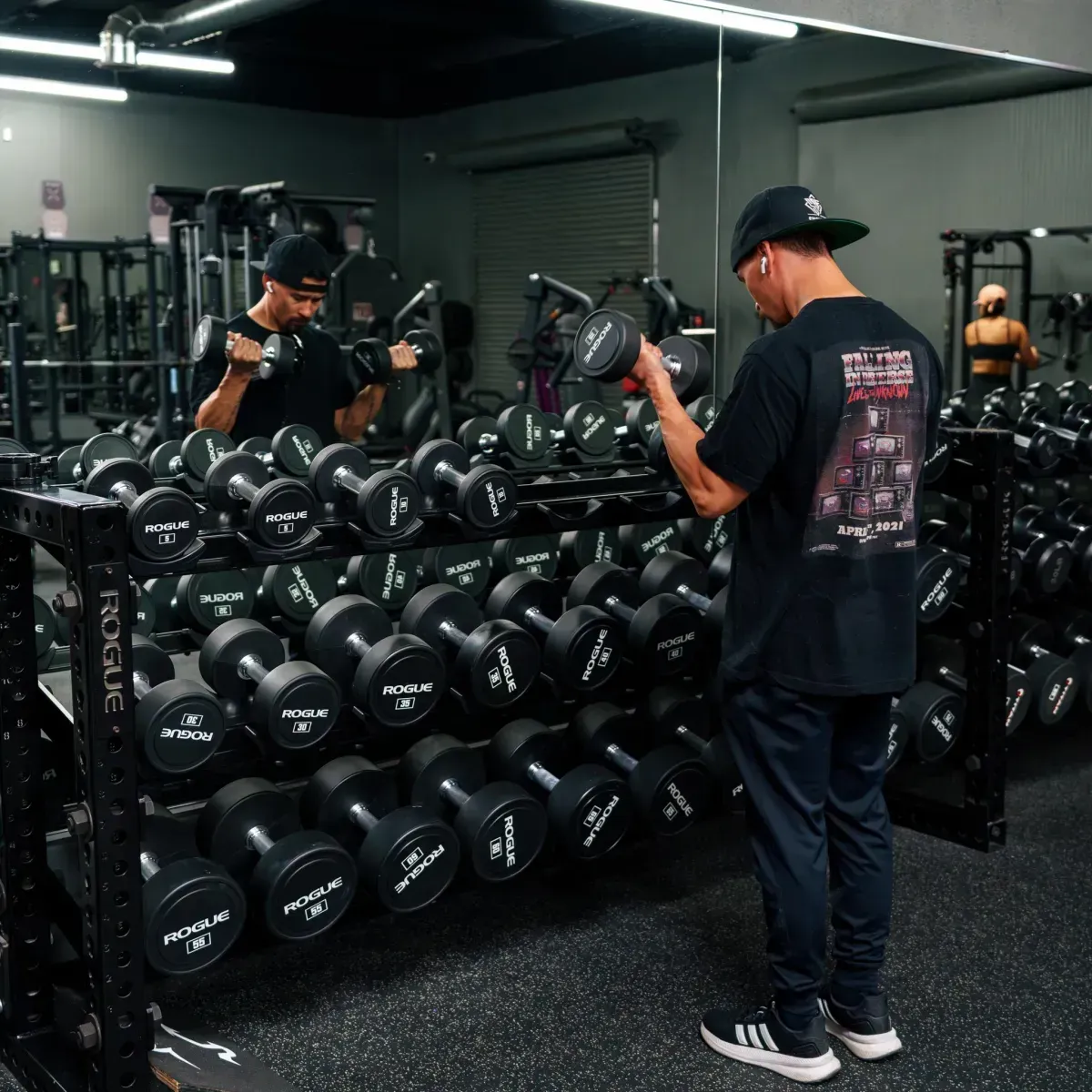 Gym member doing arm curls in the private gym near the dumbbell rack