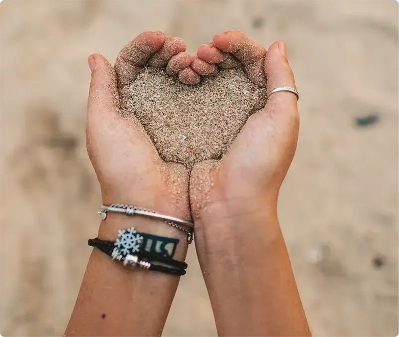 Hands holding sand in shape of heart.