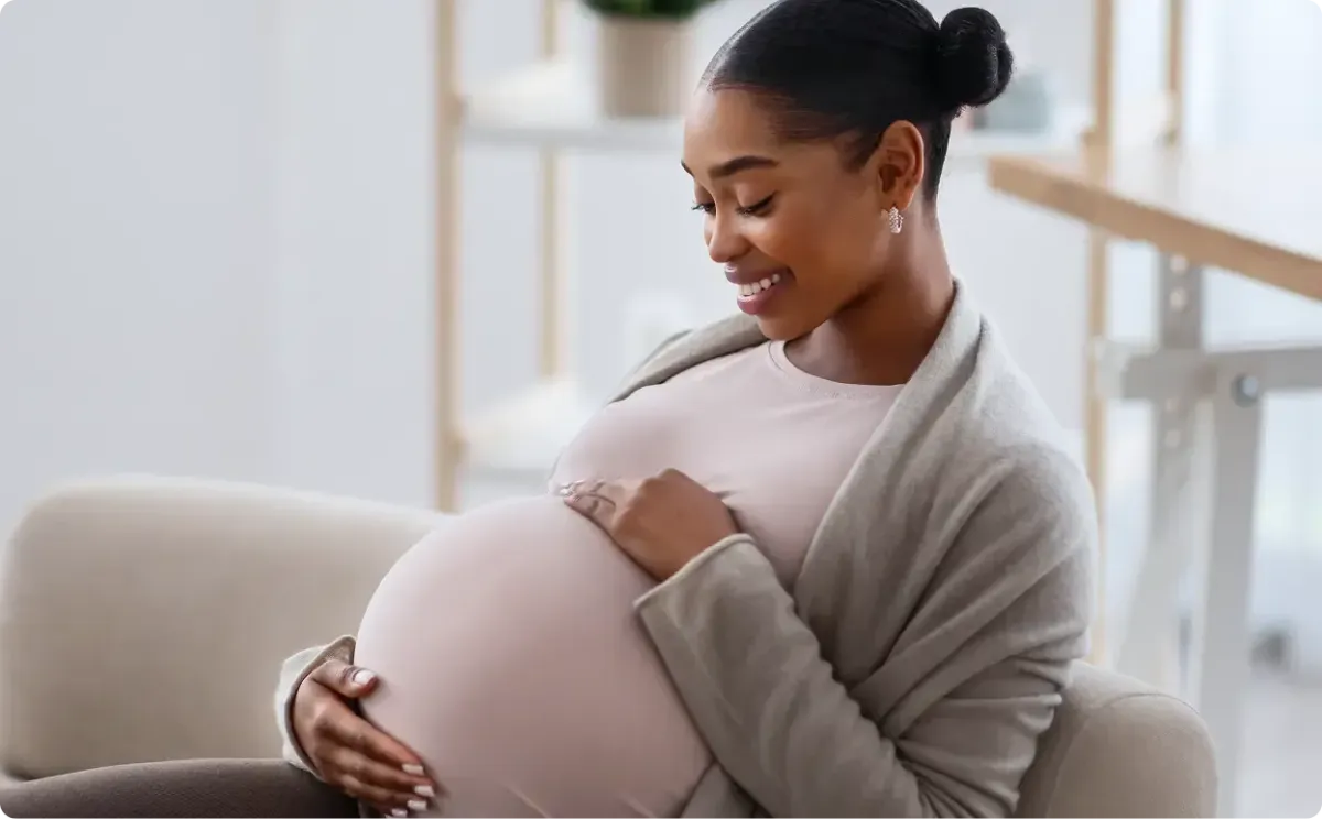 Pregnant woman smiling on couch because of fertility treatment.