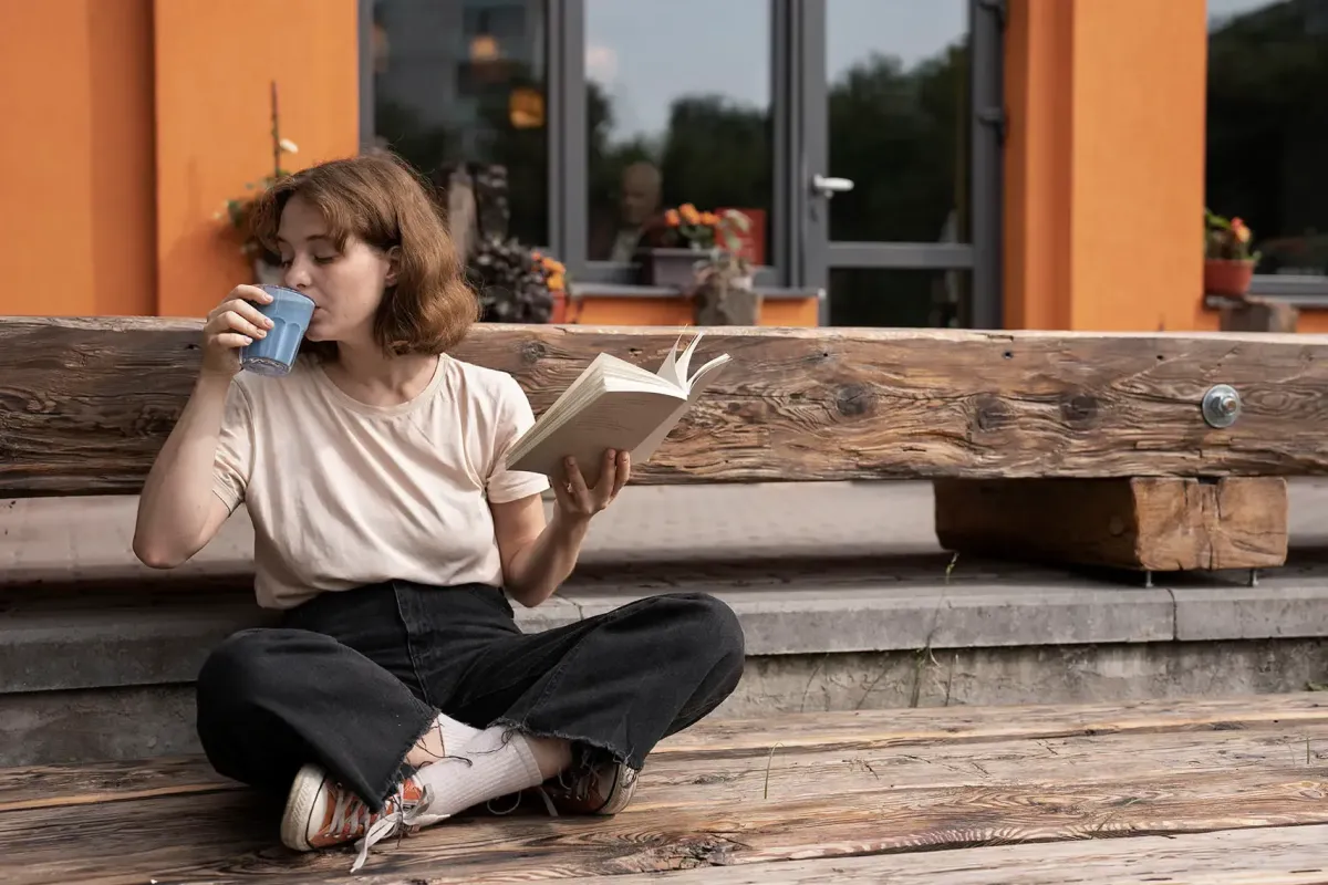 Female relaxing outdoors while reading a book and drinking coffee.