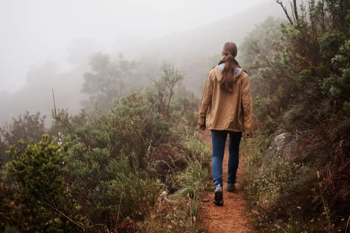 Woman walking on path in the foggy forest.