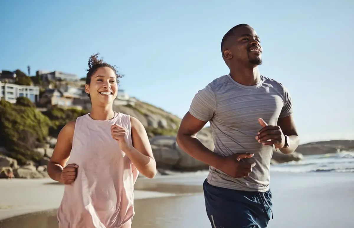 Active couple smiling and running on the beach.